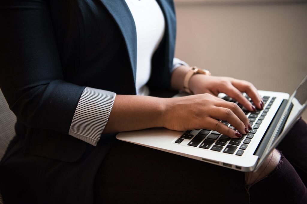 Woman in a blazer typing on a laptop in a well-lit room, focused on remote work.