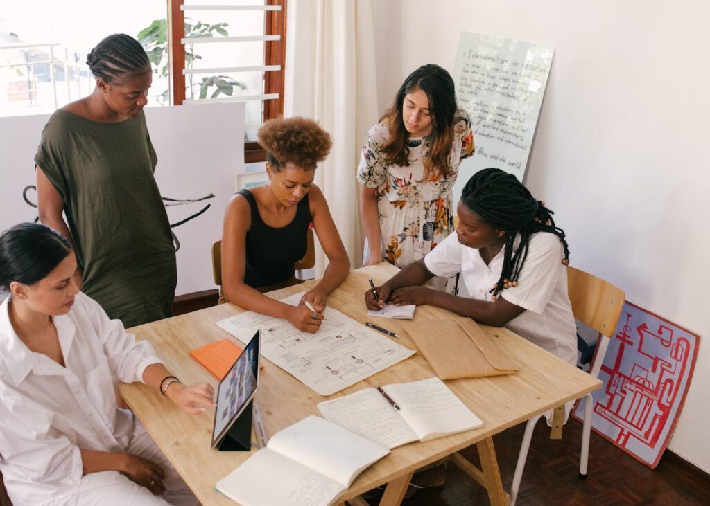 Diverse team collaborates on a project using digital and paper resources in a bright office.